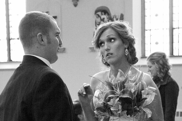 A black and white Funny Wedding Photos image of a bride looking surprised while talking to the groom.