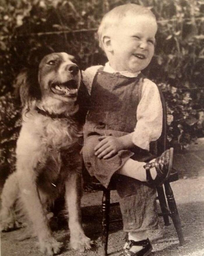 A vintage photo of a laughing baby sitting next to a dog, capturing animals stealing the spotlight.