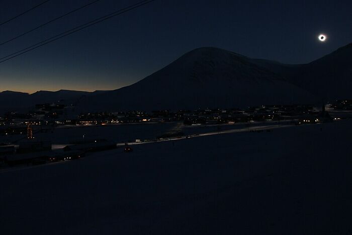 Extraordinary solar eclipse photo over a snowy town and mountains, a historic capture.