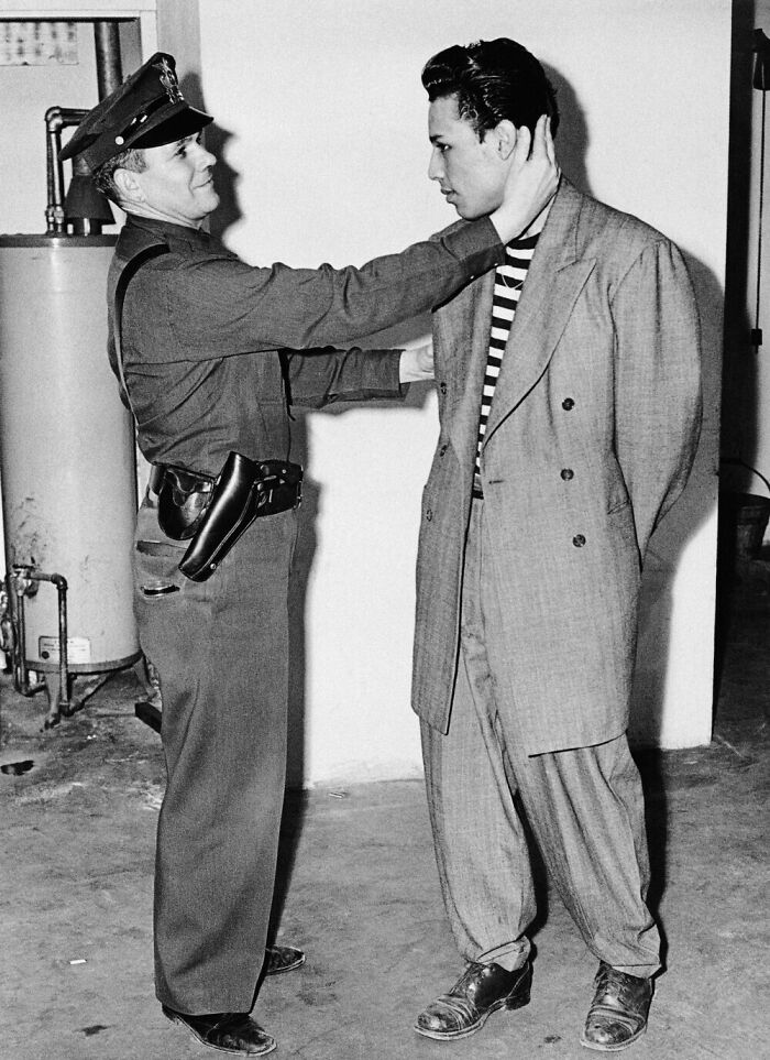 A black and white photo of a police officer frisking a man in a zoot suit, a rare image from American history.
