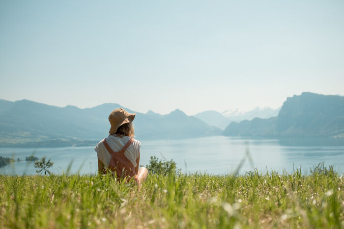 A person sits on a grassy hill, overlooking a lake and mountains, contemplating life and what comes after.