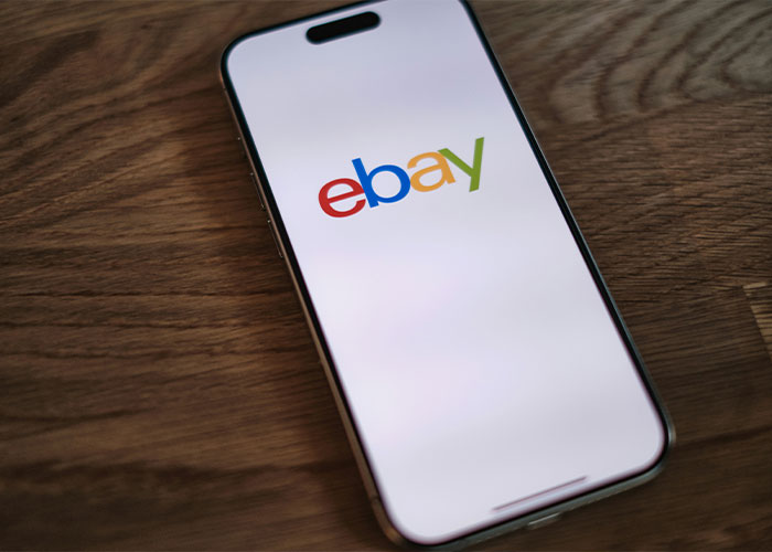 A close-up of an iPhone displaying the eBay logo, symbolizing the eBay karma for the old couple's lives.