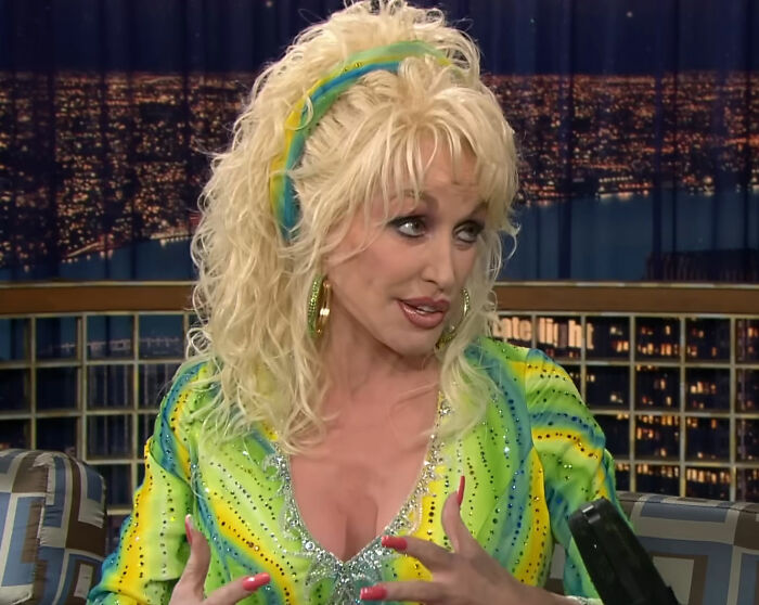 Dolly Parton in a vibrant green and yellow outfit during an interview, discussing her secret illness and hospital admission.