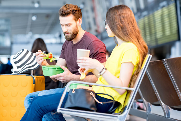 A couple eating a packed meal in an airport, highlighting a poverty habit of bringing your own food.