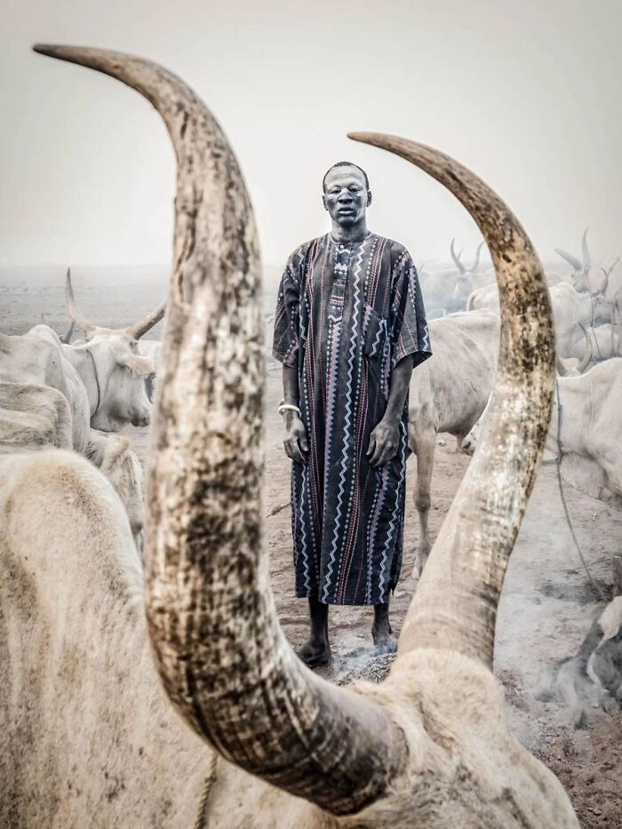 A young boy with a dirt-covered face crouches on the ground, creating shapes from mud. This image won a 2026 European Photography Award.
