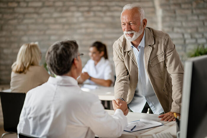 An older man shakes hands with a professional, a secret possibly shared in this confidential encounter.