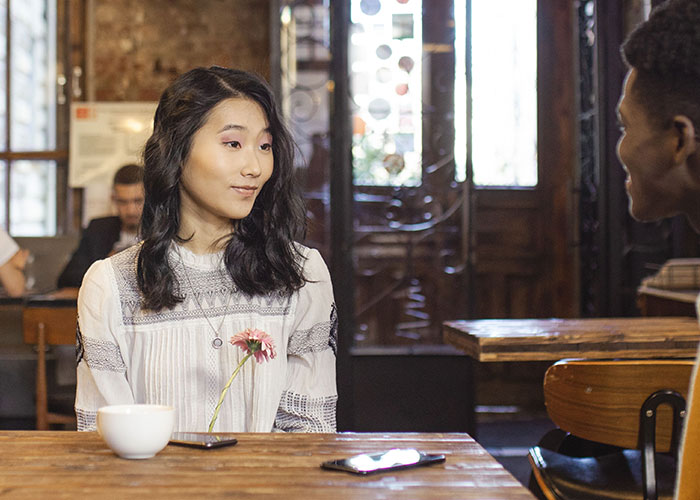 Woman smiling faintly across a table, possibly on a first date with women.