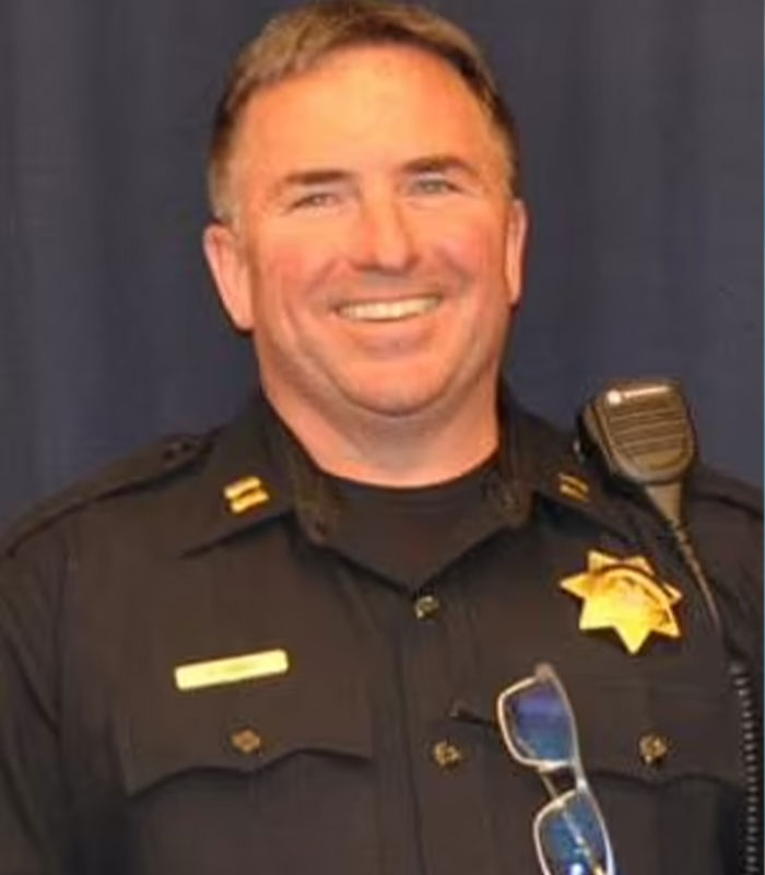 A smiling police officer in uniform, illustrating the legal repercussions and karma against eBay after the campaign to ruin an old couple's lives.