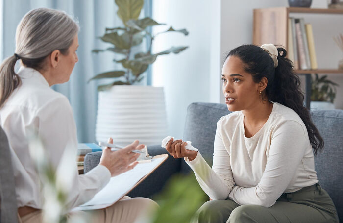 A young woman speaking to her therapist, holding a tissue, discussing why she walked out without her therapist.