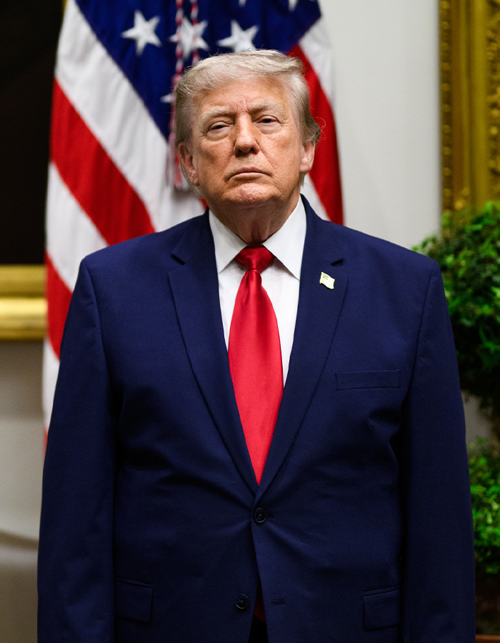 Donald Trump in a blue suit and red tie, standing in front of an American flag, regarding Trump rumors.