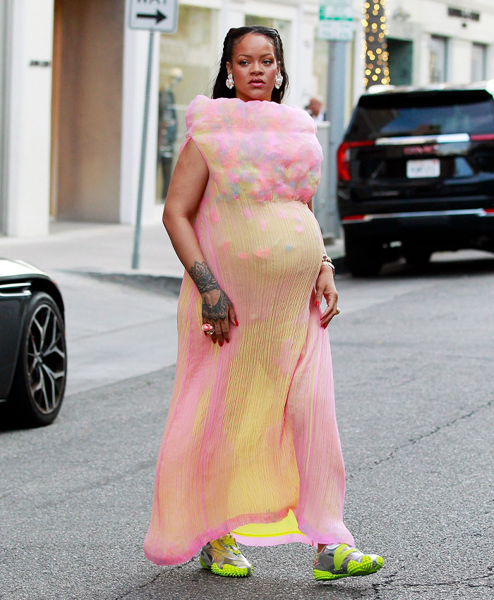 Rihanna in a vibrant pink and yellow flowy dress, confidently displaying her celebrity pregnancy look.