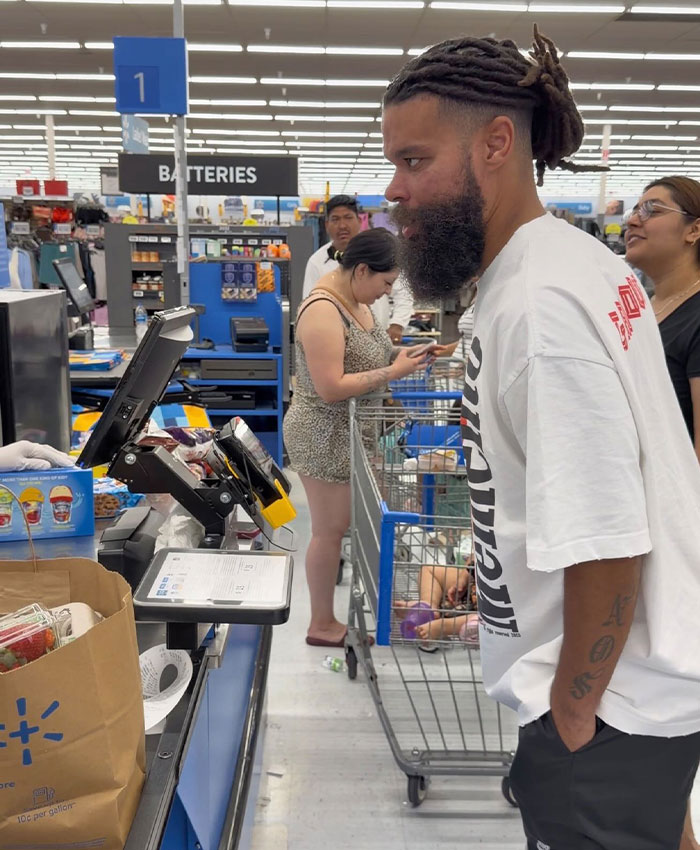 Influencer with dreadlocks and a beard standing at a Walmart self-checkout, in a scenario leading to a lifetime ban.