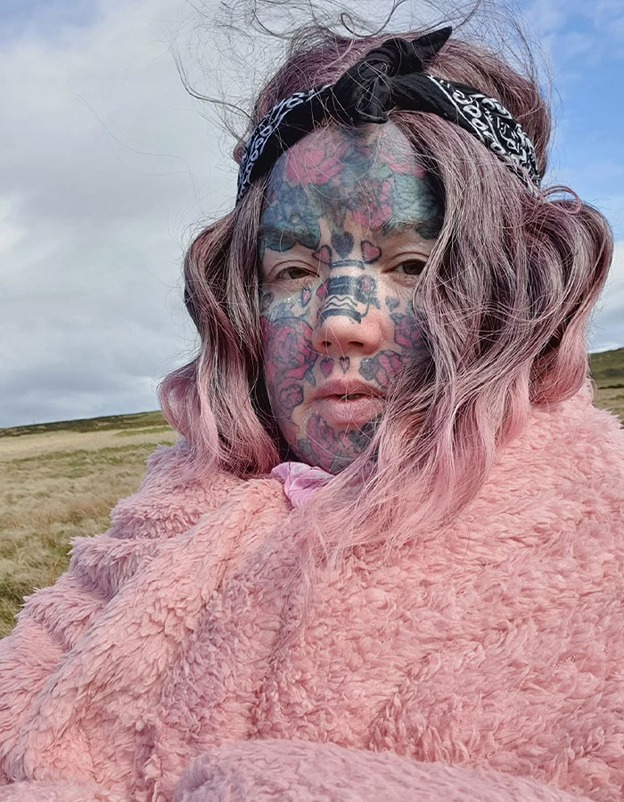 A mom with 800 tattoos shows her face without the extreme look outdoors, with pink hair and a fluffy coat. A mom with 800 tattoos shows her face without the extreme look outdoors, with pink hair and a fluffy coat.