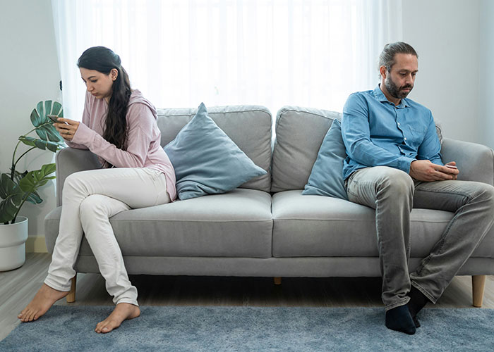 A couple on a couch with distance between them, looking at phones, symbolizing how the 72-hour rule divides couples. A couple on a couch with distance between them, looking at phones, symbolizing how the 72-hour rule divides couples.
