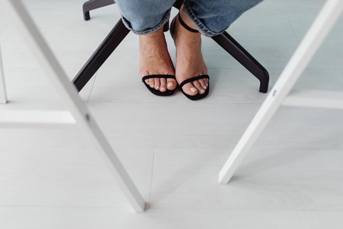 A person's feet in black high heels and jeans, symbolizing dumb work rules.