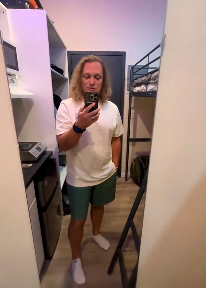 A man takes a selfie in his 90-square-foot NYC apartment, showcasing the compact urban living space. A man takes a selfie in his 90-square-foot NYC apartment, showcasing the compact urban living space.