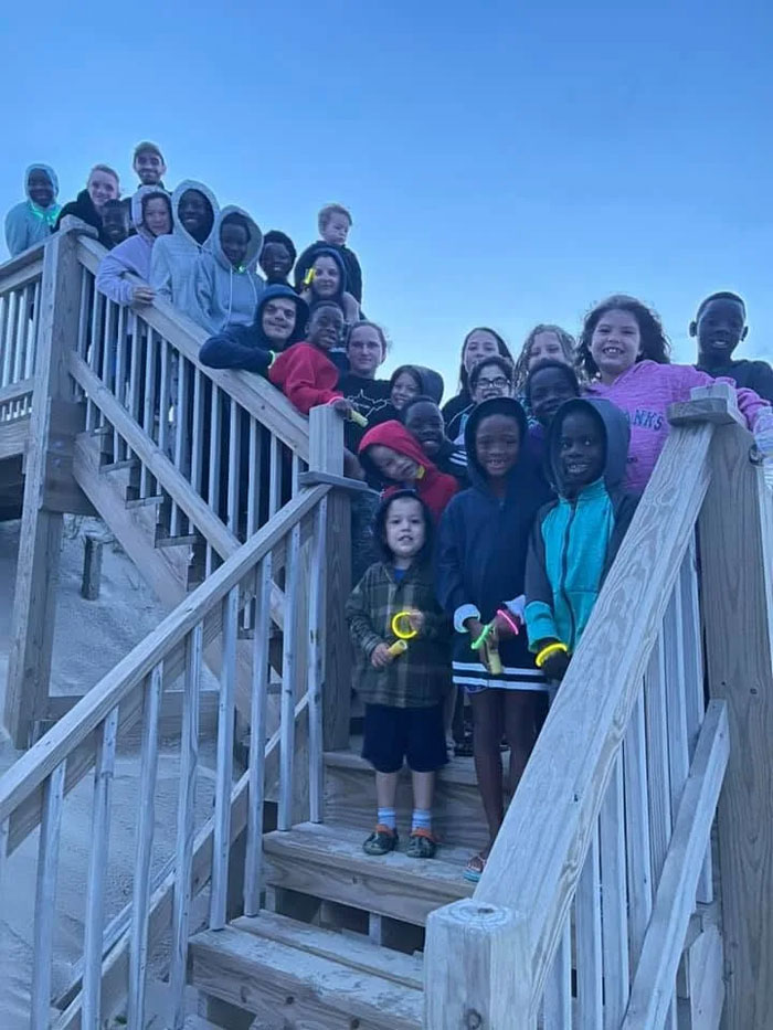 A group of children from a family of 39 smiling on a wooden staircase outdoors. A group of children from a family of 39 smiling on a wooden staircase outdoors.