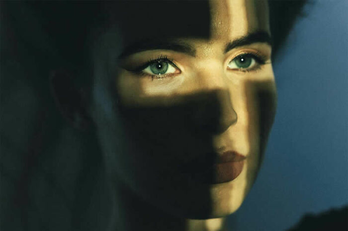 A woman with intense green eyes partially lit by a beam of light, part of cinematic portraits.