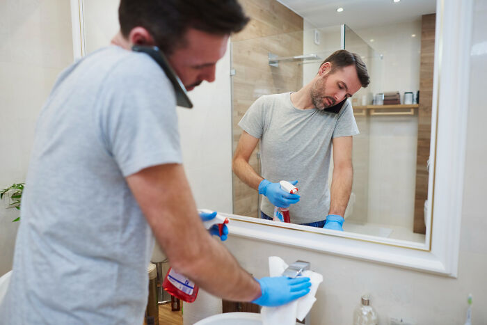A man multi-tasking by cleaning a bathroom sink while on a phone call, symbolizing dumb reasons couples divorce.