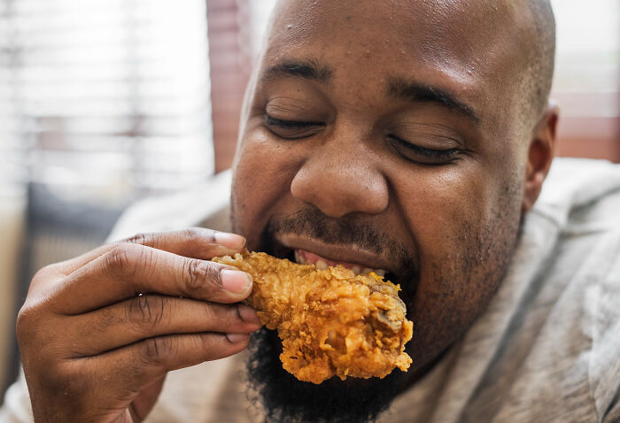 A man happily eats a piece of fried chicken, one of the things doctors refuse to do themselves.
