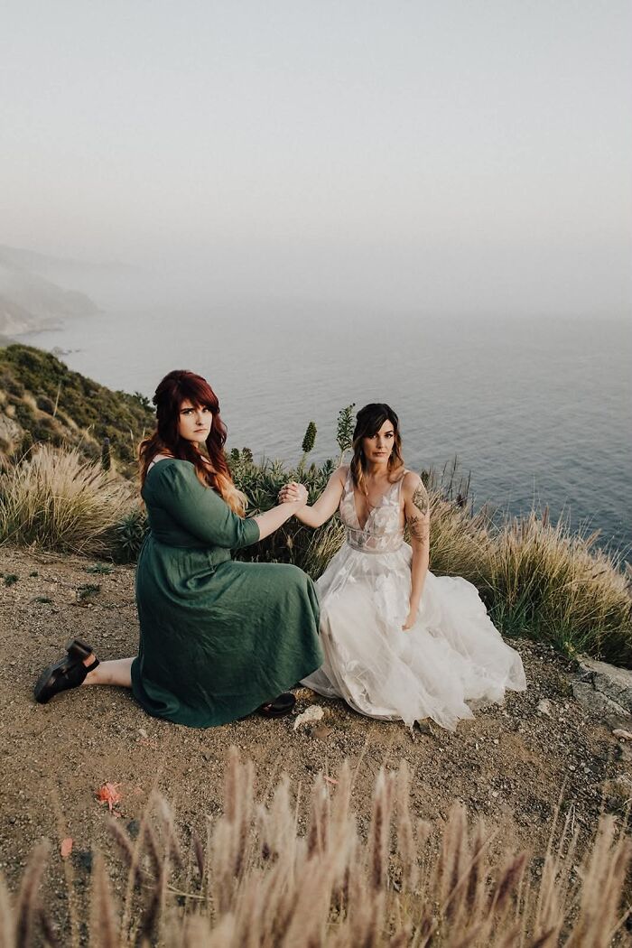 Two women pose on a cliff overlooking the ocean, an iconic and funny wedding photo.