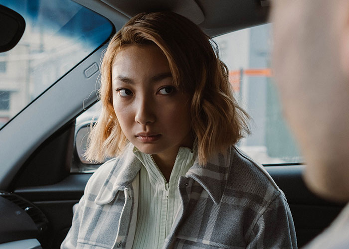 A woman in a car with a plaid jacket and a skeptical expression, reflecting on worst first dates.