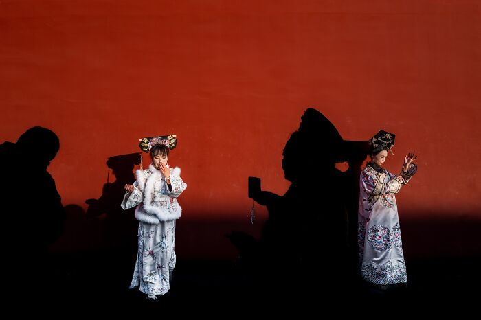 Best street photos from the Macadam Awards: Two women in traditional dress against a red wall with large shadows.