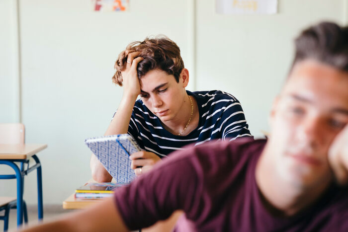 A tired student in a striped shirt holds their head, contemplating a secret they'd never confess in class.