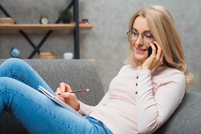 A woman on her couch on the phone, taking notes in a journal. She walked into therapy and walked out without her therapist.