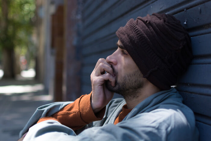 A man in a beanie sits outdoors, deep in thought, with his hand near his mouth, revealing a secret.
