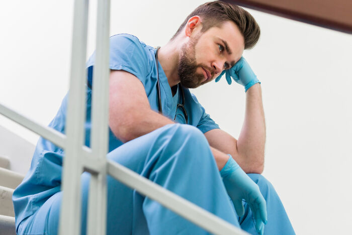 A male doctor sits on stairs looking sad, having delivered hard diagnoses.