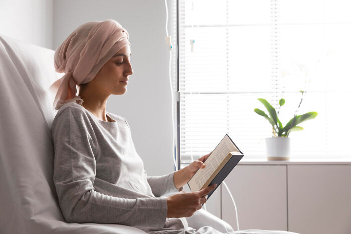 Woman with a headscarf reading in a hospital bed, finding peace in her life.