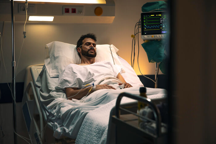 A man in a hospital bed with medical tubes and monitoring equipment, looking weak. This image relates to dumb reasons couples divorce.