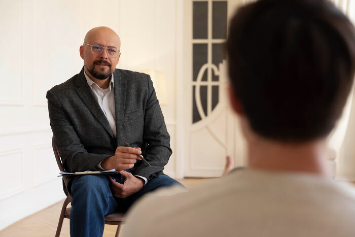 A therapist sits opposite a client in a bright room, discussing therapy experiences and why people leave therapy.