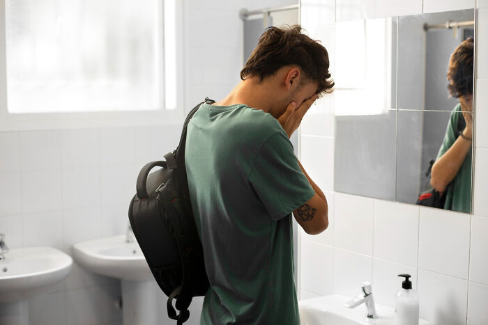 A man with his face in his hands, standing in a bathroom, revealing a secret burden.