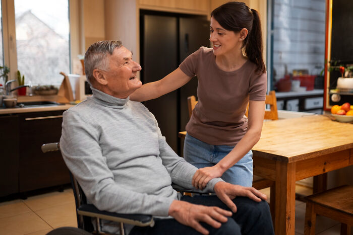 A young woman helps an older man in a wheelchair, a silent secret might be held between them.