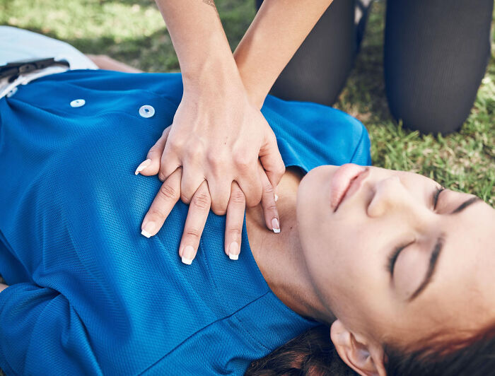 Person performing CPR on another person lying on grass, a life-changing skill to pick up.