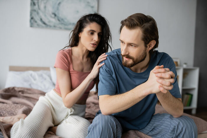 Woman comforting a sad man in bed, showing emotional struggles that can be reasons couples divorce.