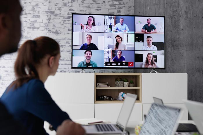 Two employees look at a screen displaying a video conference with multiple people, illustrating dumb work rules.