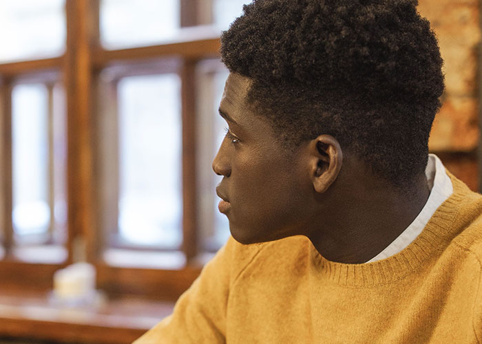 A man in a yellow sweater looking intently out a window, perhaps thinking about his worst first dates.
