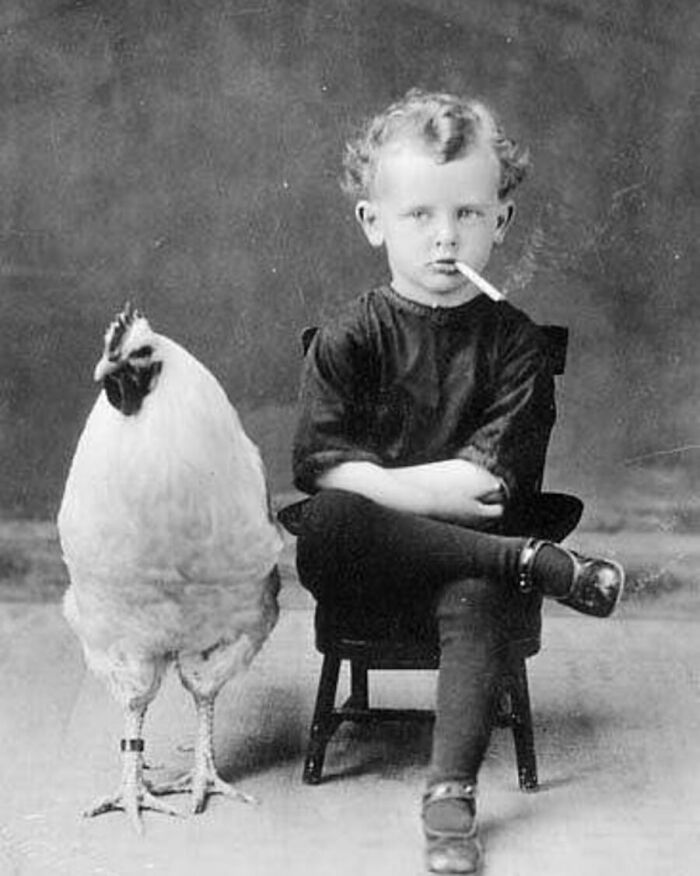 Vintage photo of a boy smoking next to a rooster, capturing animals stealing the spotlight.