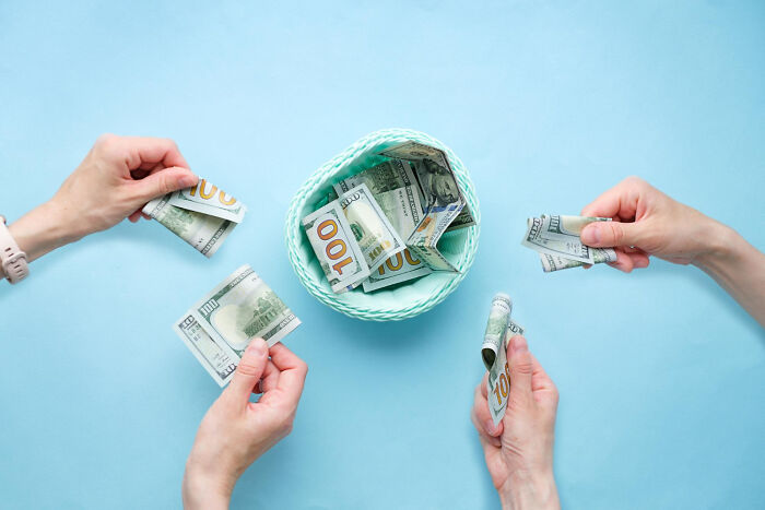 Four hands holding dollar bills around a basket of money, representing employee stories about getting fired.