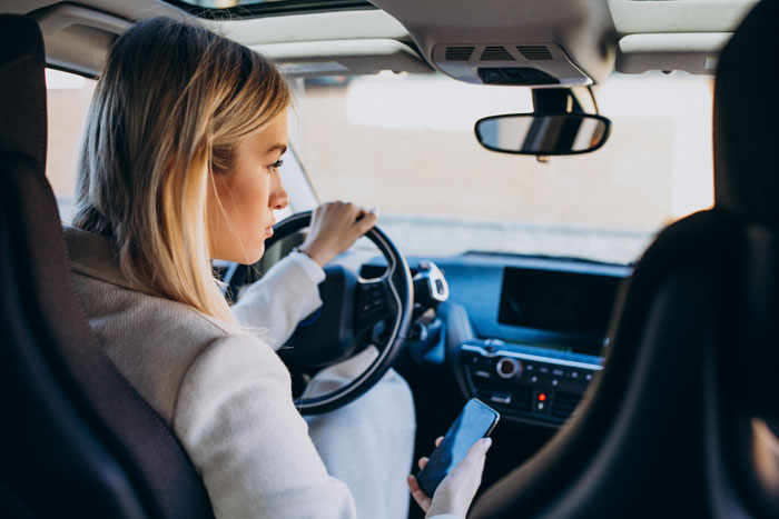 A woman is driving a car while looking at her phone, representing the couple's niece. A woman is driving a car while looking at her phone, representing the couple's niece.