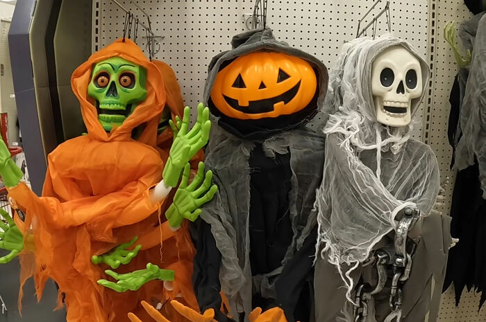 Various Halloween costume decorations, including a pumpkin, skeleton, and green figure, on display at a store.