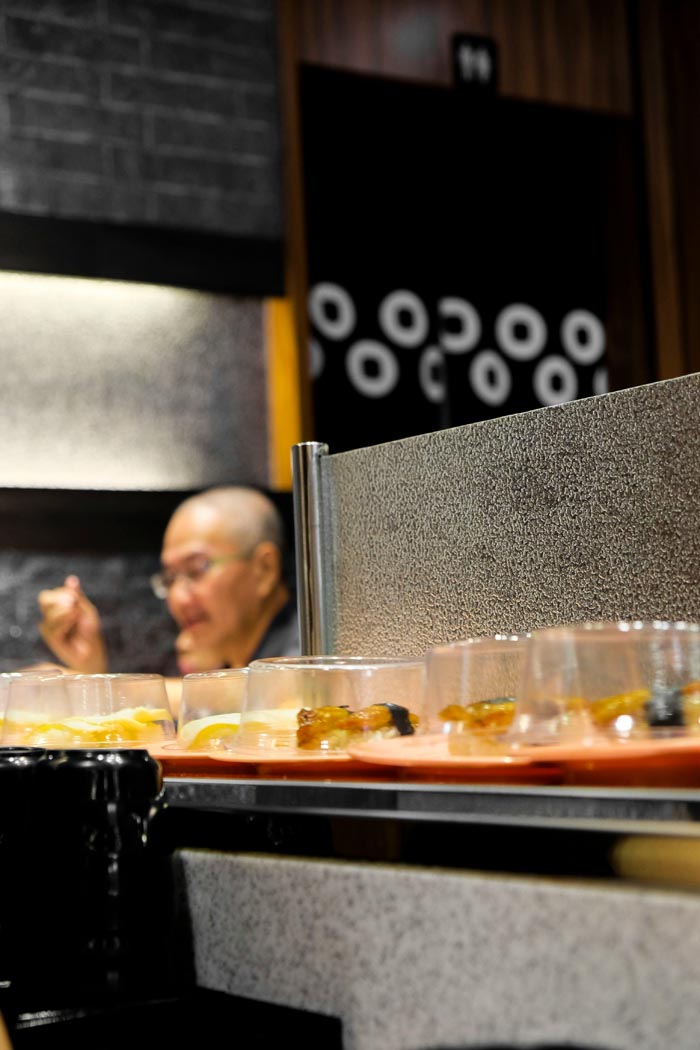 A man eating in a restaurant with sushi passing on a conveyor belt, illustrating dumb work rules.
