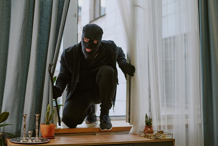 Burglar breaking into a home through a window, a reason couples divorce due to financial stress.