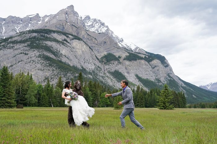An iconic and funny wedding photo with a groom, bride, and Bigfoot in a scenic mountain setting.