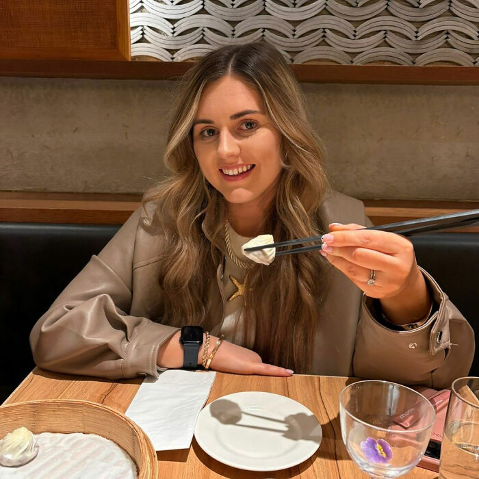 A woman smiling while eating, showcasing reasons shes put off having kids. A woman smiling while eating, showcasing reasons shes put off having kids.