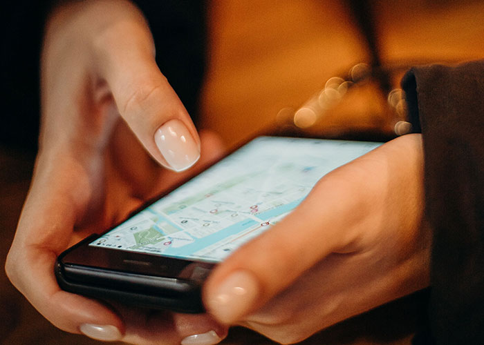 A woman's hands using a smartphone with a map on the screen, possibly navigating a first date.