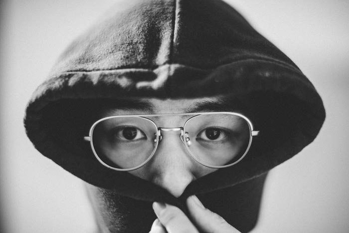Close-up of a person with glasses wearing a hoodie, with part of their face covered, implying dumb work rules.